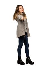 A full-length shot of a Teenager girl with coat points finger at you with a confident expression on isolated white background