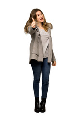 A full-length shot of a Teenager girl with coat giving a thumbs up gesture because something good has happened on isolated white background