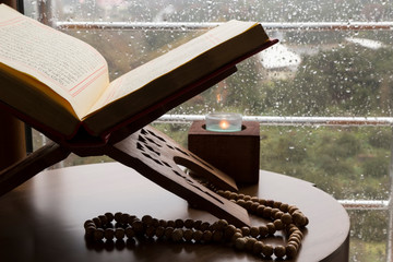 Quran and rosary beads on the wooden background with candle for Islamic concept. Holy book Koran...