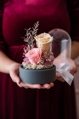 Womans hands holding long-lasting roses in a glass dome