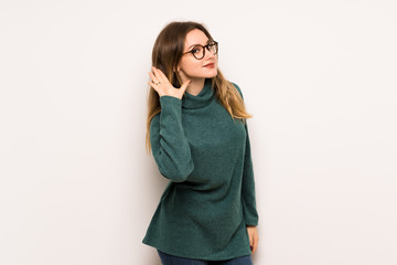 Teenager girl over white wall listening to something by putting hand on the ear