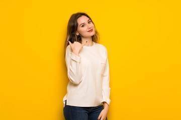 Teenager girl over yellow wall making phone gesture. Call me back sign