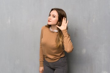 Teenager girl over textured wall listening to something by putting hand on the ear
