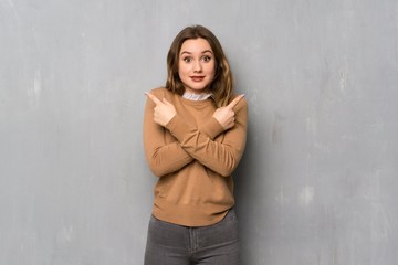 Fototapeta premium Teenager girl over textured wall pointing to the laterals having doubts