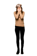 Full-length shot of Young woman with beret is a little bit nervous and scared putting hands to mouth on isolated white background