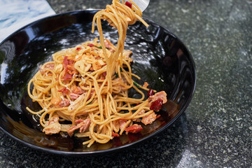 Spicy and chili spaghetti with with bacon in black pan and fork