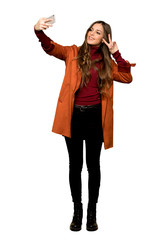 Full-length shot of Young woman with coat happy and pointing the mobile on isolated white background