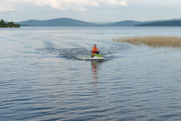 A young man in a life jacket rides a water bike on a lake in summer.