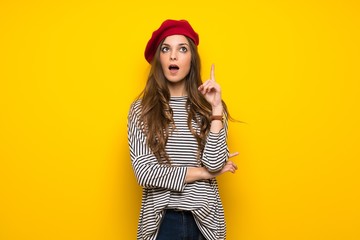 Girl with french style over yellow wall thinking an idea pointing the finger up