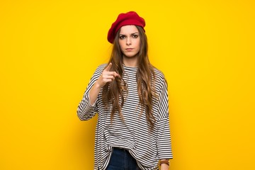 Girl with french style over yellow wall frustrated by a bad situation and pointing to the front