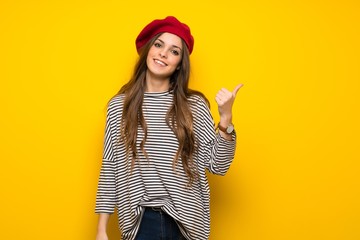 Girl with french style over yellow wall pointing to the side to present a product