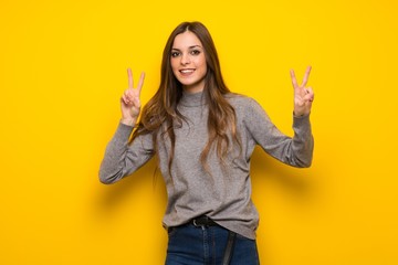 Young woman over yellow wall smiling and showing victory sign with both hands