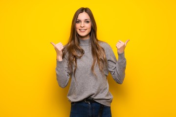 Young woman over yellow wall giving a thumbs up gesture with both hands and smiling