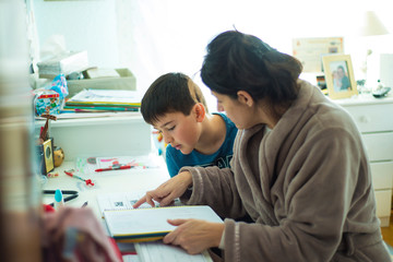 Madre ayudando a su hijo a estudiar y hacer los deberes o tareas escolares en casa - obrazy, fototapety, plakaty