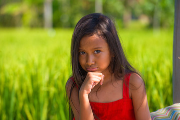 Fototapeta premium sweet shy and beautiful 7 or 8 years old child in cute red Summer dress having fun outdoors smiling cheerful at rice field in young girl enjoying holidays and nature