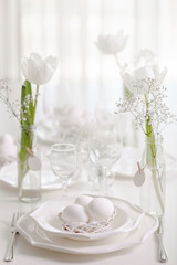Happy Easter! Decor and table setting of the Easter table with white tulips and dishes of white color.