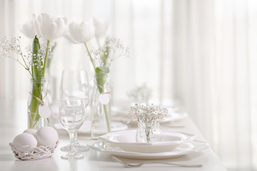 Happy Easter! Decor and table setting of the Easter table with white tulips and dishes of white color.