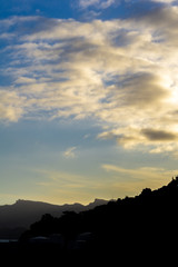 White clouds over mountains peaks, dramatic sunset with black foreground 