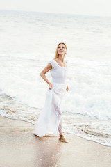 Fototapeta na wymiar Attractive happy mature tourist blonde woman in long white dress on asian sand tropical beach.