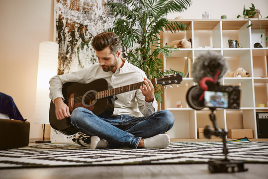 My inspiration. Bearded male music blogger sitting on the floor and holding the guitar, while recording new video for his vlog