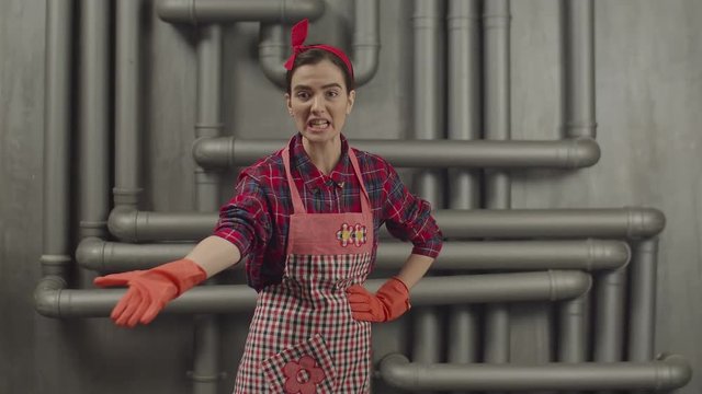 Irritated overworked housewife in apron and protective gloves scolding someone for mess in house, expressing frustration and anger. Furious housekeeper woman making rebuke and gesturing aggressively.
