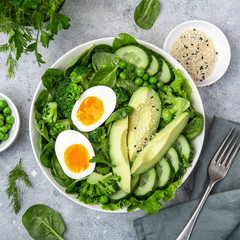 healthy green salad with avocado, eeg, broccoli, cucumber, green peas and spinach in white  bowl