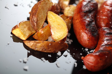 Grilled sausages.Baked potatoes .Closeup.On miroor surface.Tasty dish for beer