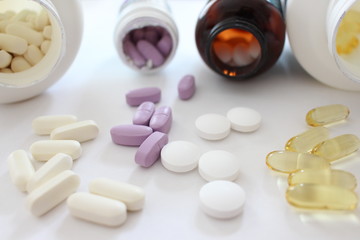A close up photograph of medication, a variety of pills and tablets spilling out of medication bottles, against a white background