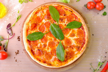 Salami pizza with spinach leaves served on wooden board on the table. Close-up top view.
