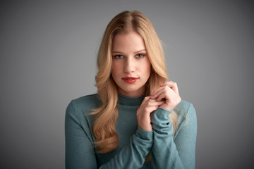 Portrait of blond hair young woman looking at camera and smiling while posing at light grey background