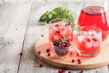 Refreshing drink with cranberries, ice and rosemary on white wooden background, selective focus, copy space