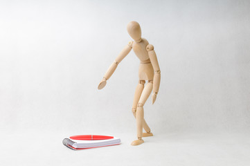 Wooden doll taking a pen on a notepad