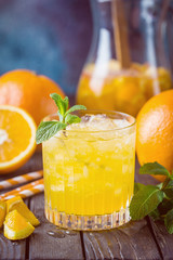 Glass jar of fresh orange juice with ice and fresh fruits on dark table.