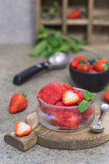 Delicious strawberry ice cream in a glass bowl with fresh strawberries on wooden cutting board