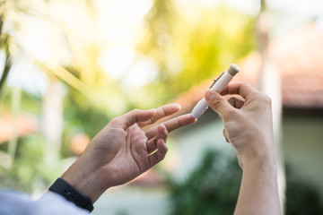 Close up of asian man's hands using lancet on finger to check blood sugar level by glucose meter, Healthcare medical and check up, diabetes, glycemia, and people concept