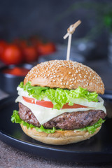 Hamburger with beef meat burger and fresh vegetables on dark background. Tasty fast food.