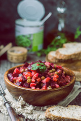 Russian beetroot salad vinaigrette in wooden bowl with rye bread, rustic background
