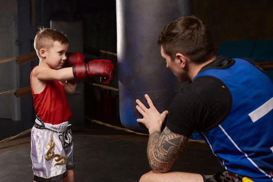 Trainer teaching a kid how to hit punches. Kid wearing boxing gloves and head guard training with his coach inside a boxing ring
