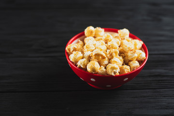 popcorn with caramel in a red plate on a black wooden background