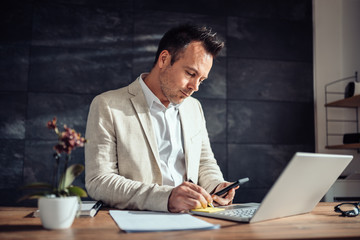 Fototapeta premium Businessman holding smart phone and writing on a adhesive notes