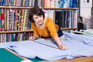 Female seller measuring and cutting off piece of textile