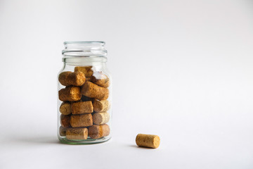 Wine corks lie in a glass jar on a white background.