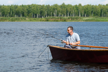 man sits in a boat and catches fish by spinning on the river