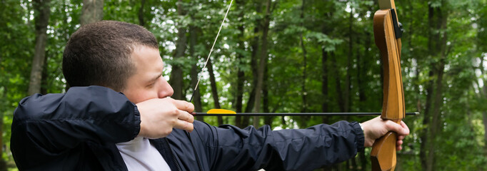 man pulls a bow string for a shot in the forest, close-up, long photo