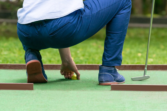 minigolf player pulls a yellow ball out of the hole, rear view, close-up