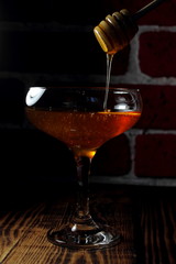 Honey flows from a wooden spoon into a glass goblet.