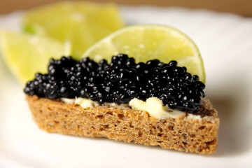 Black caviar and a slice of lime on a piece of bread on a plate close-up