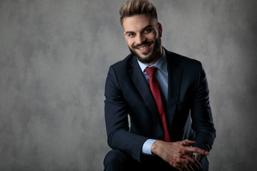 laughing young businessman holding elbow on knee and palms together