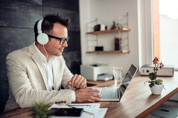 Obraz na płótnie Canvas Businessman using laptop and listening music on headphones