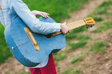 musical concept of little young teen girl holding denim vintage guitar outdoors
